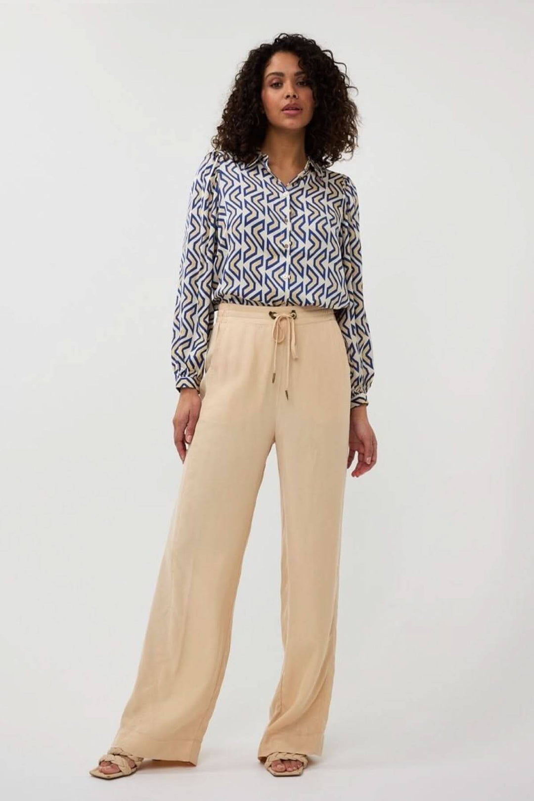 Chemise fluide à motif géométrique bleu et beige, associée à un pantalon clair, style décontracté.