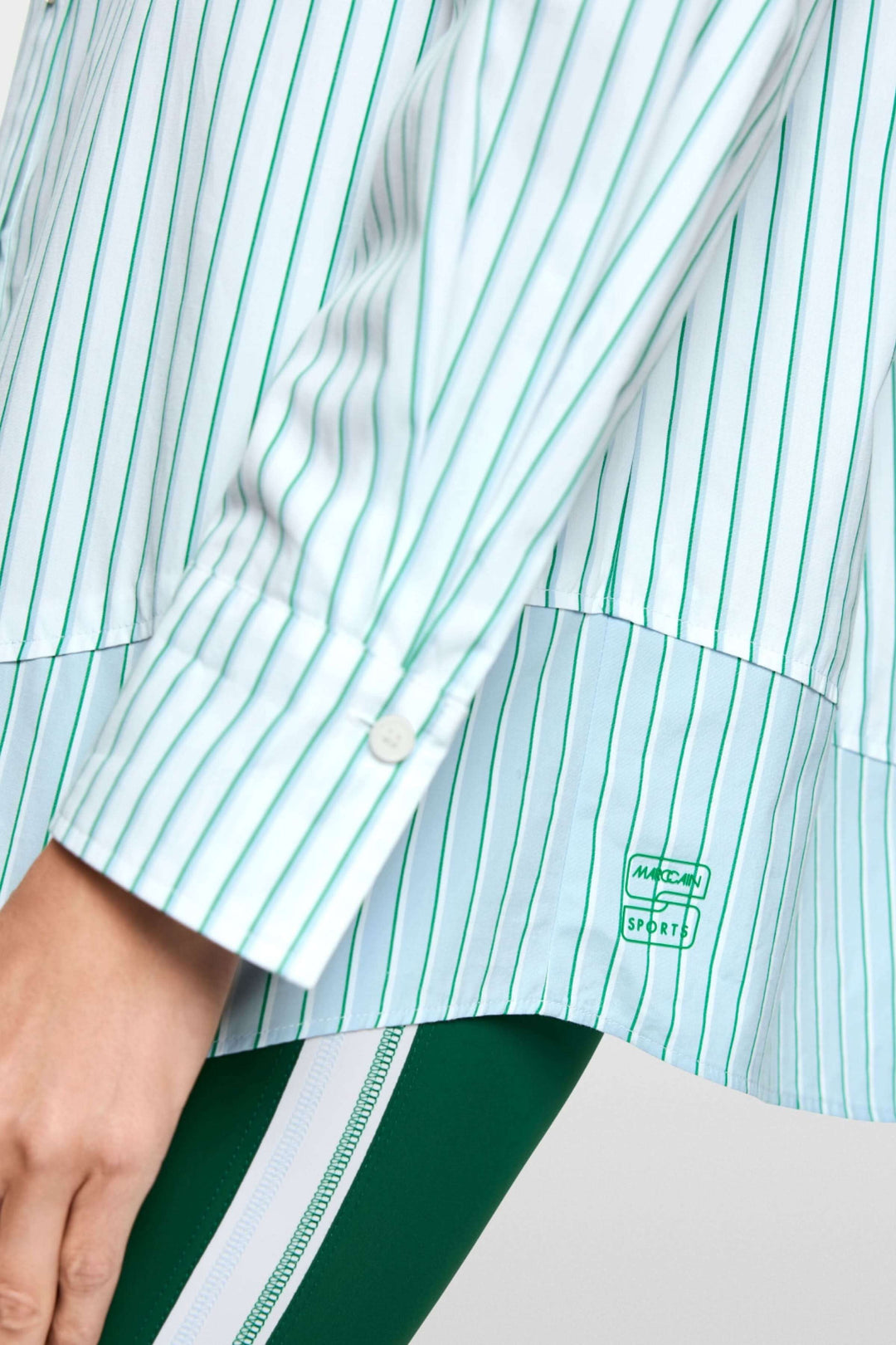 Chemise rayée en coton avec manches longues et design moderne, détenteur en bas à droite visible, portée sur un pantalon vert foncé.