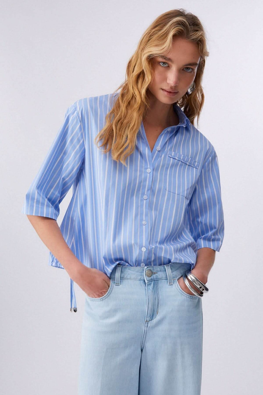 Femme portant une chemise rayée à manches courtes bleue, style décontracté et moderne, avec détails élégants et col classique.