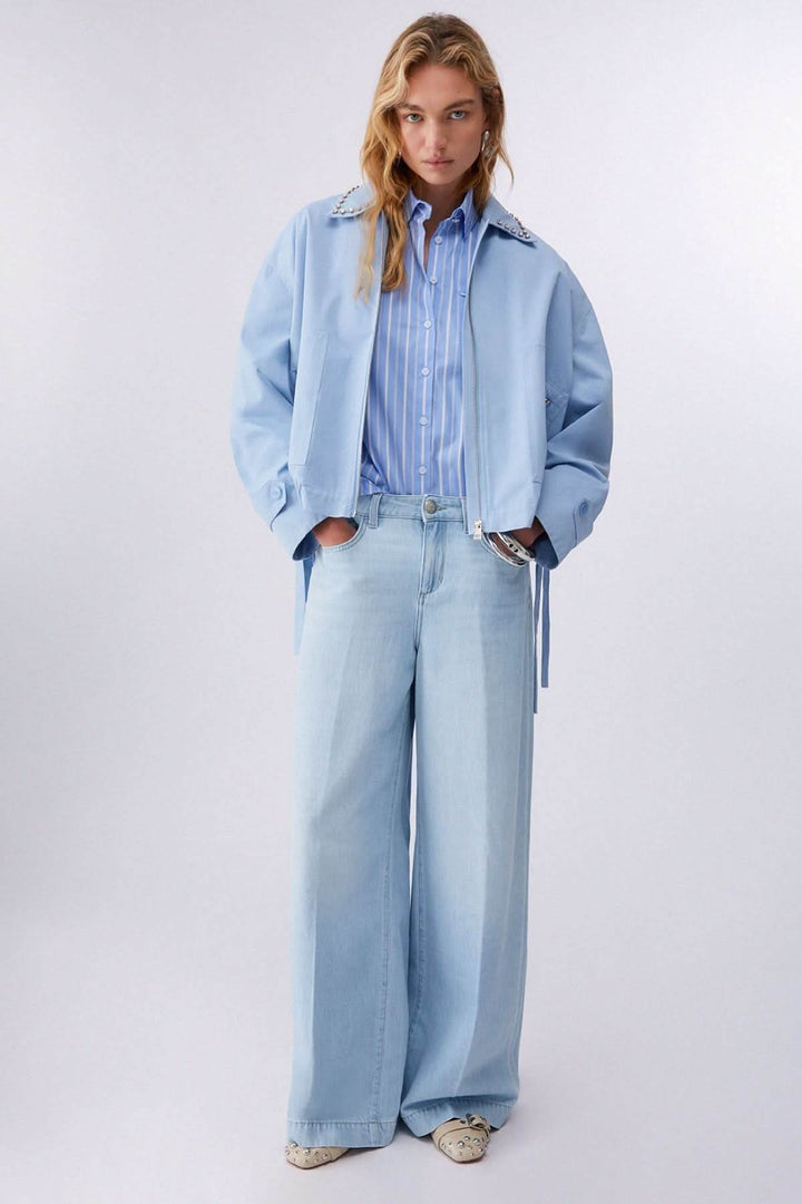 Chemise rayée à manches courtes bleue portée par un mannequin, ajoutant une touche moderne et décontractée à une tenue élégante.
