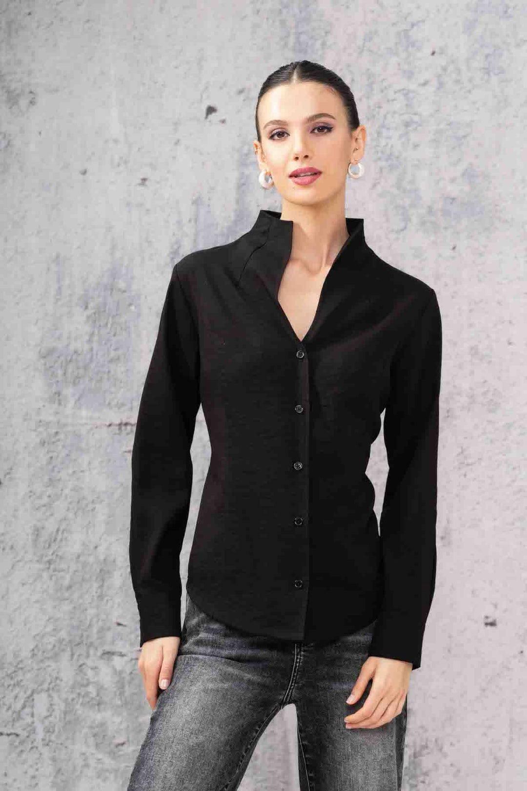 Chemise simple noire à manches longues avec col montant et boutons, portée avec un jeans.