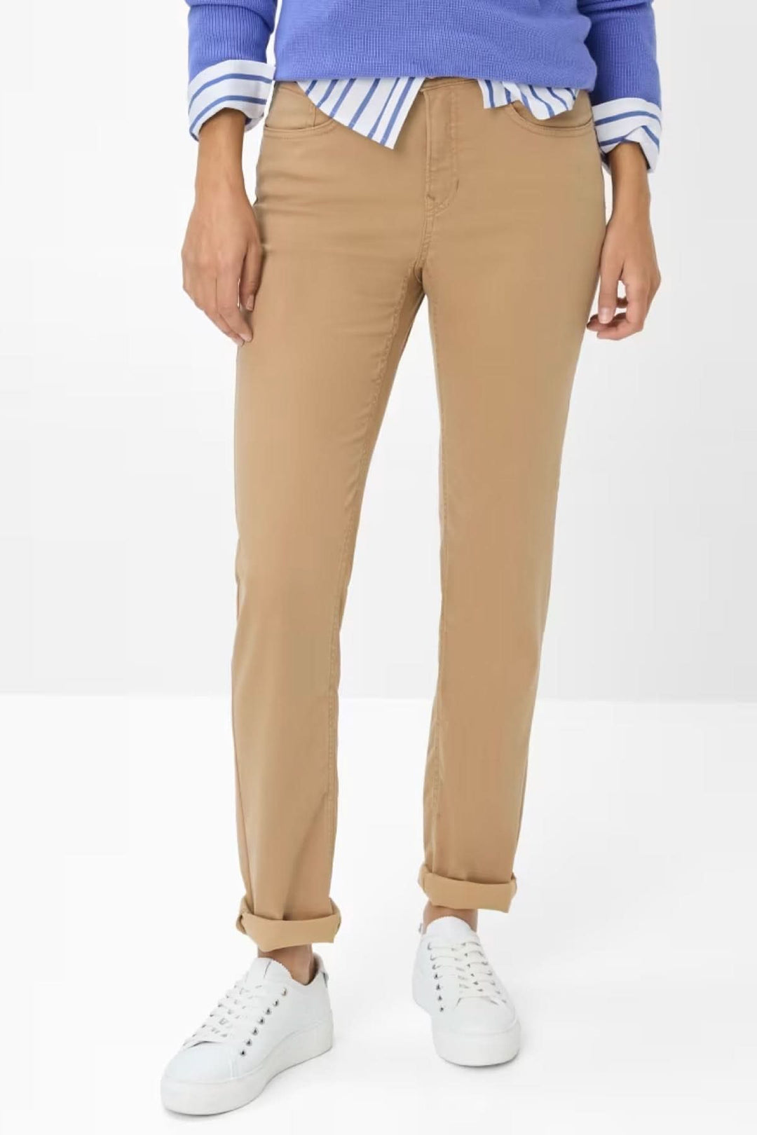 Pantalon chino ajusté camel porté avec un pull bleu et des baskets blanches, parfait pour un look casual chic.