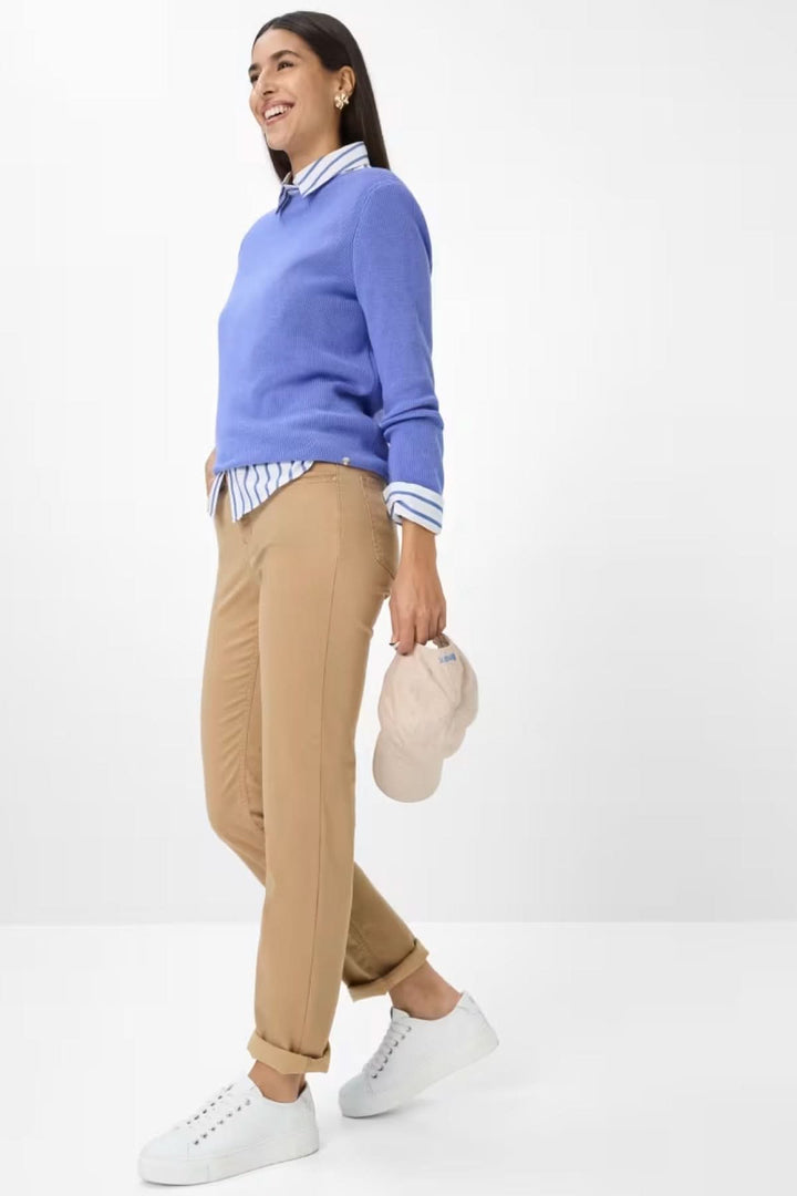 Femme souriante portant un pull bleu et un pantalon chino camel, look décontracté chic avec des baskets blanches.