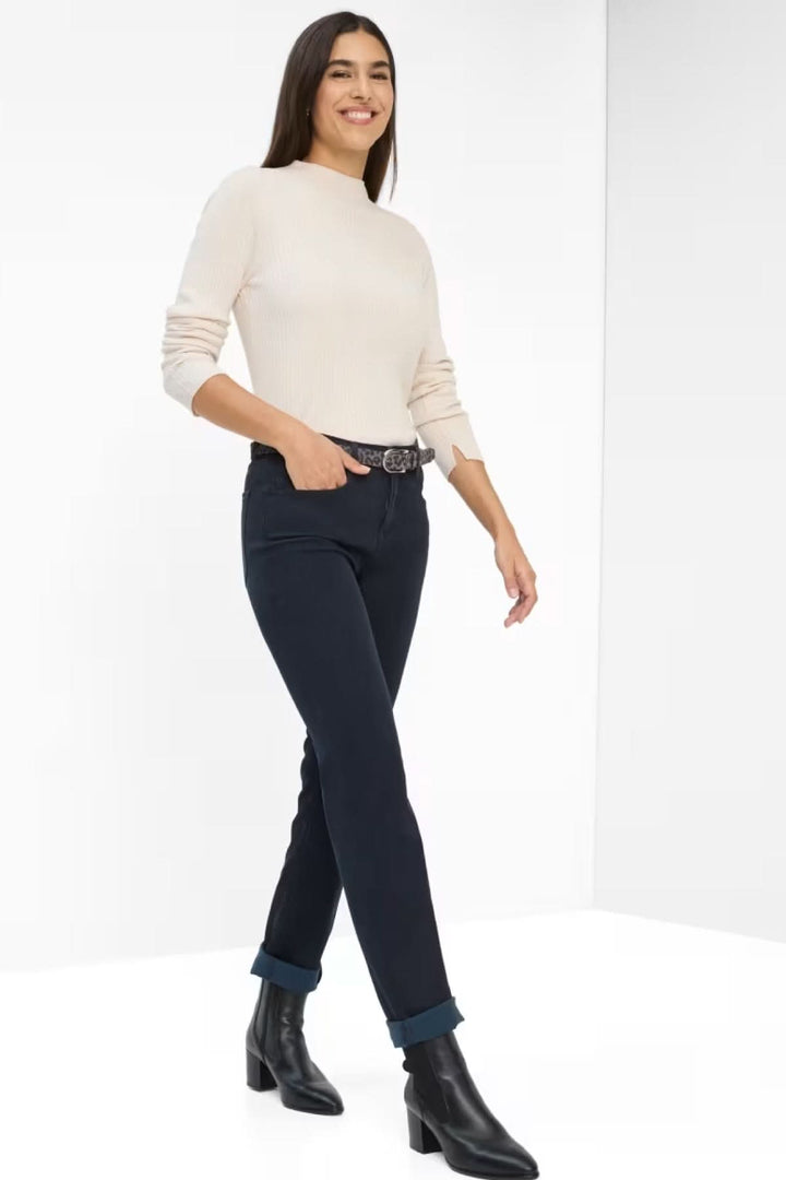 Femme en pull léger crème et jeans ajustés, marchant avec des bottines noires, style décontracté chic.