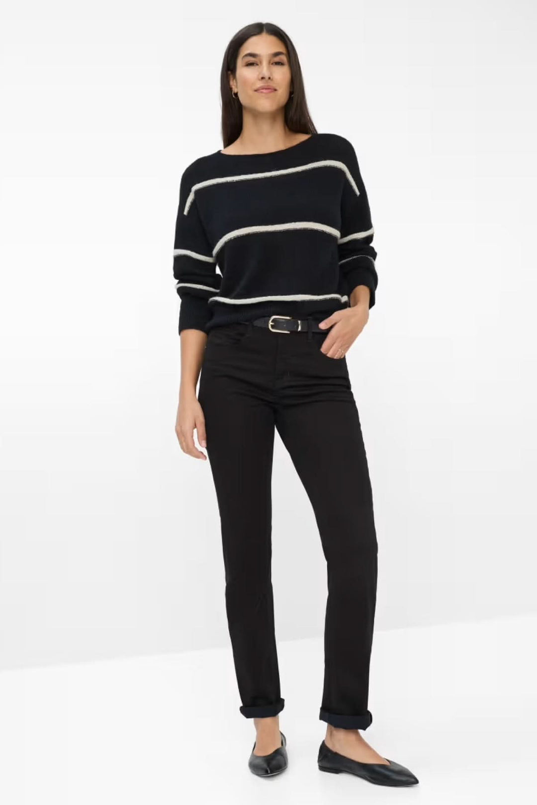 Femme portant un pull rayé noir et un pantalon chino ajusté noir, style décontracté chic.