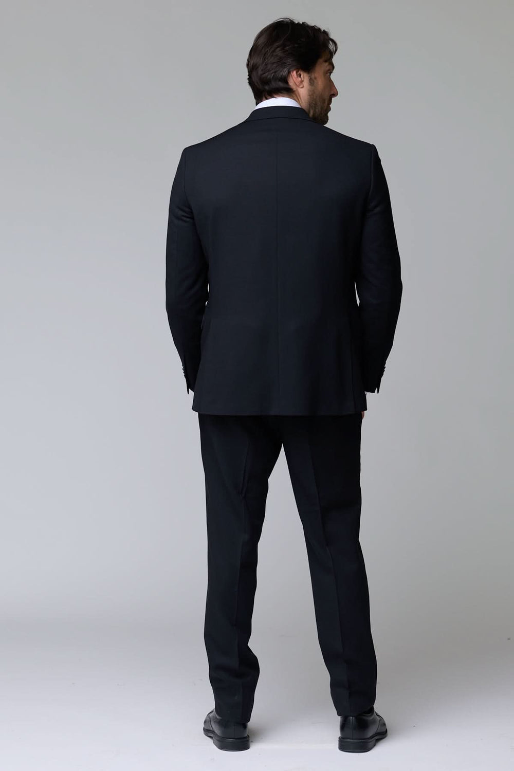 Homme portant un complet classique deux pièces noir élégant vu de dos, parfait pour des occasions formelles et le bureau.