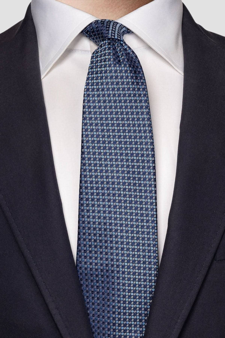 Cravate de soie bleue avec motif circulaire, portée avec une chemise blanche et un costume sombre.
