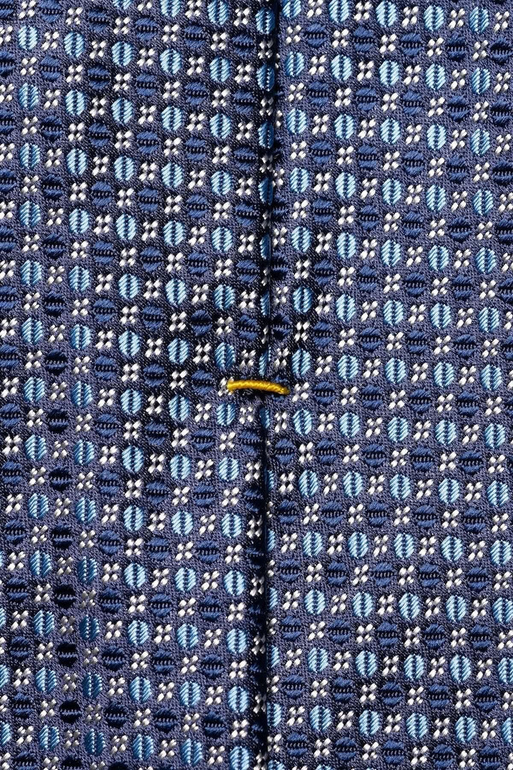 Détail du motif circulaire en bleu marine et argent sur une cravate en soie, ajoutant sophistication et élégance.