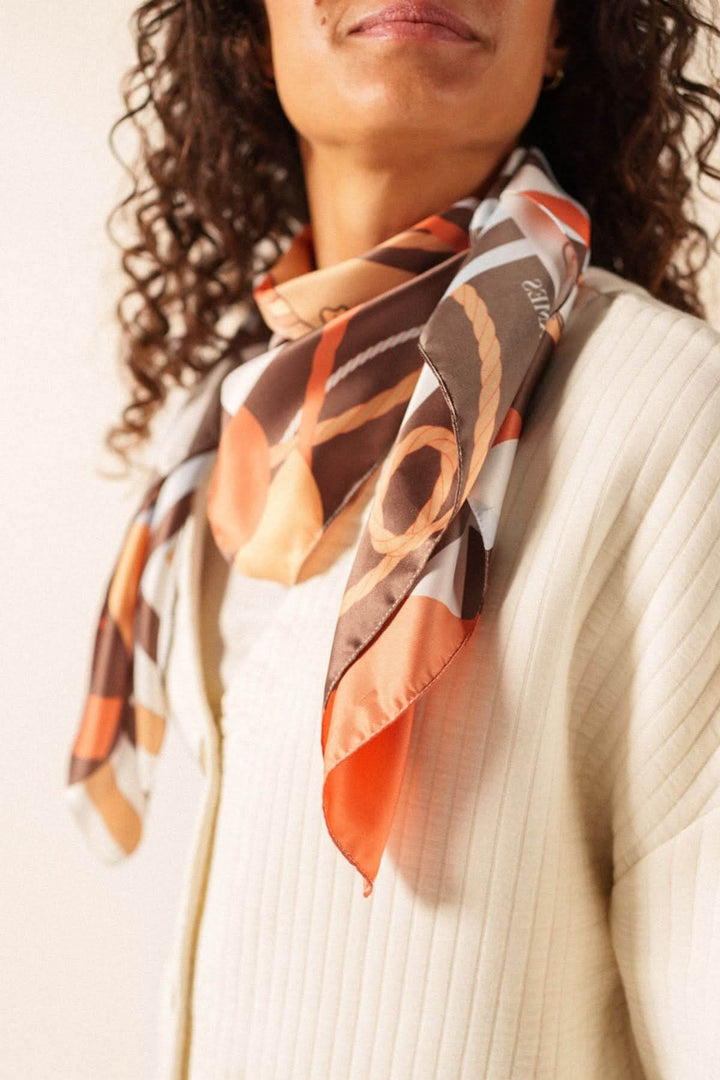 Femme portant un foulard CARRE FOND MARIN avec motif graphique, noué élégamment autour du cou, ajoutant une touche artistique à sa tenue.