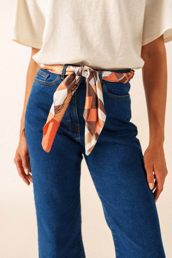 Foulard CARRE FOND MARIN noué autour de la taille avec motif graphique, ajoutant une touche stylée et artistique.