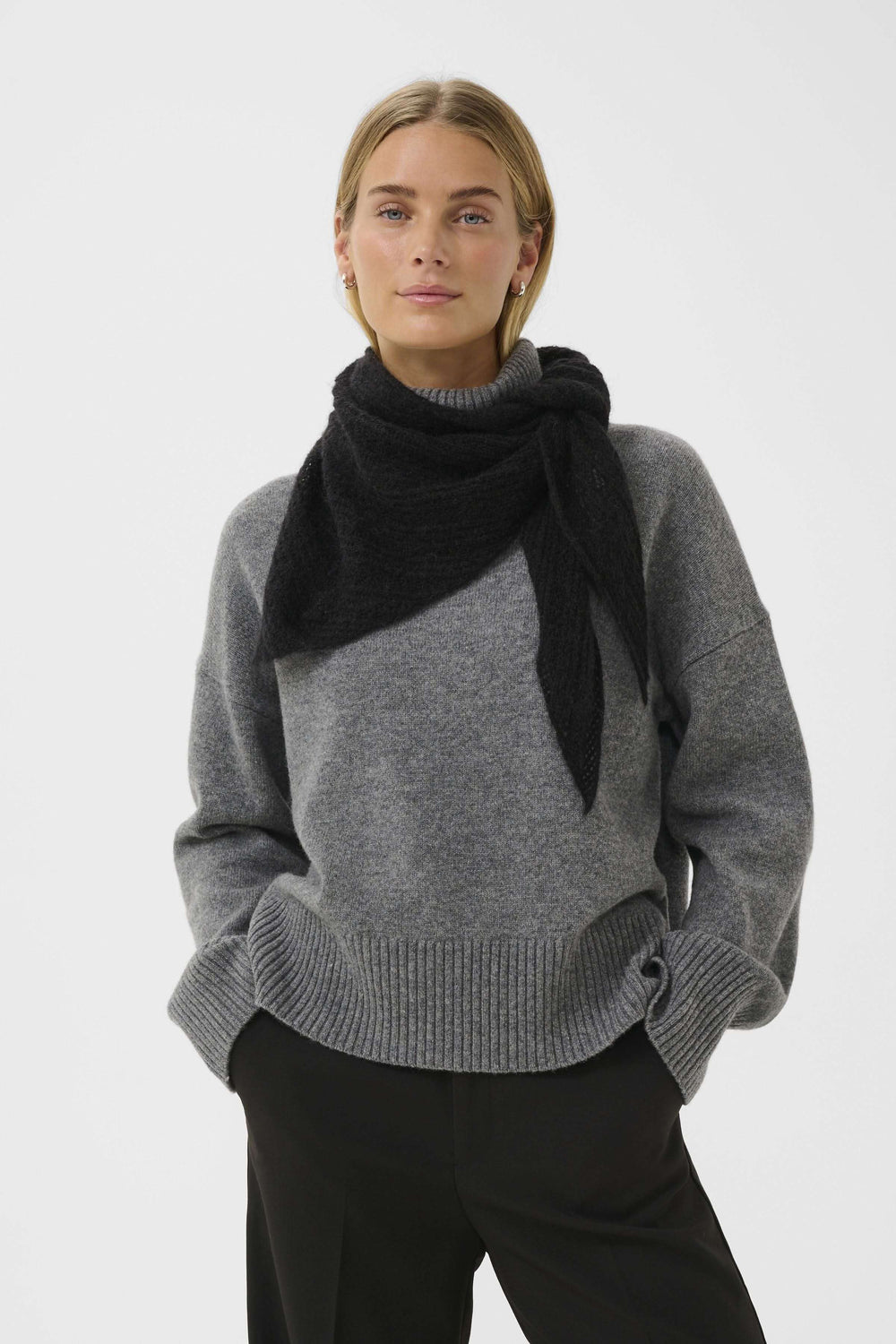 Modèle portant le Foulard Sizze noir, tricot léger et duveteux, noué sous un manteau pour un look minimaliste et moderne.