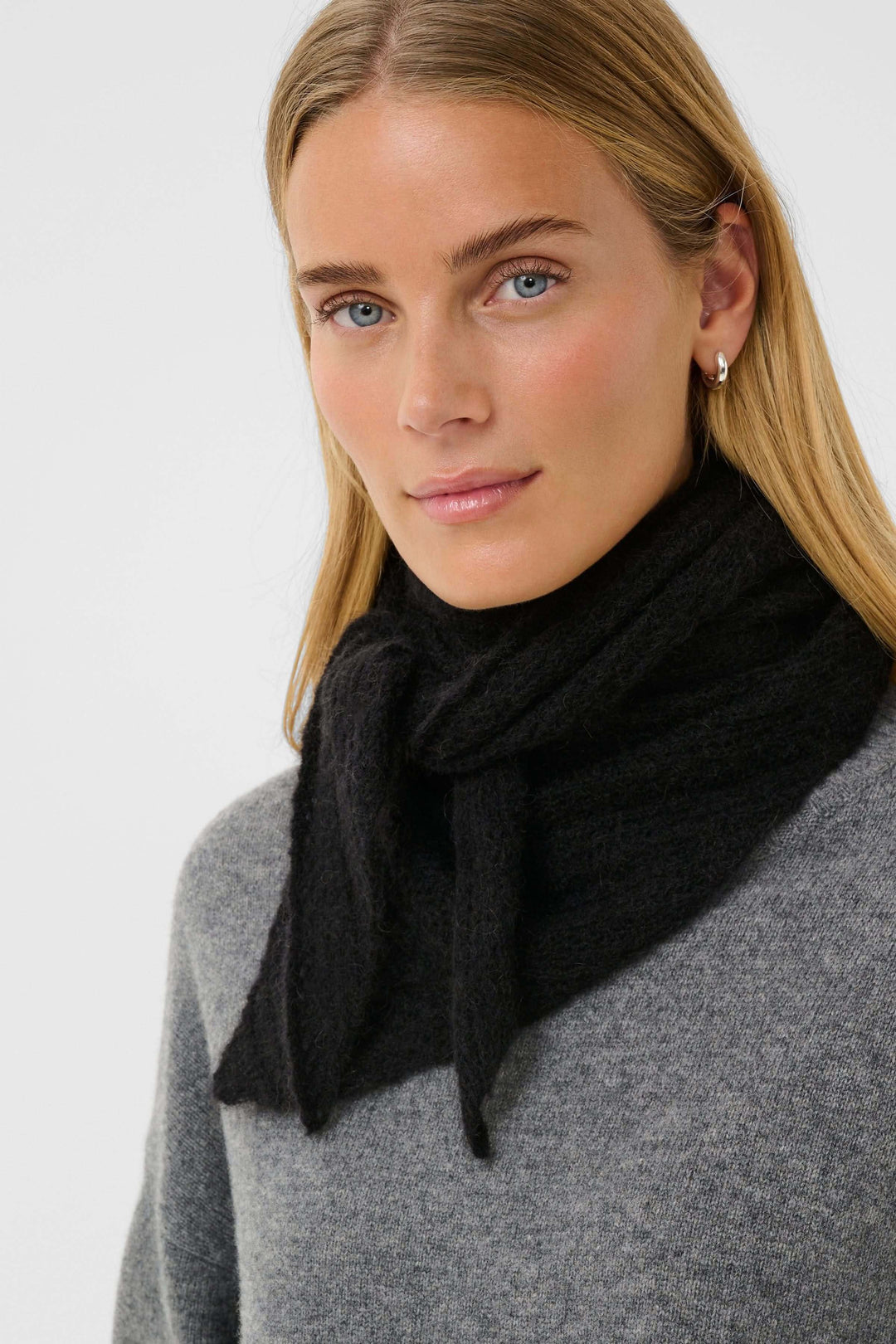 Foulard Sizze en tricot léger noir porté par une femme, ajoutant chaleur et raffinement discret. Format étroit, finition effilée.