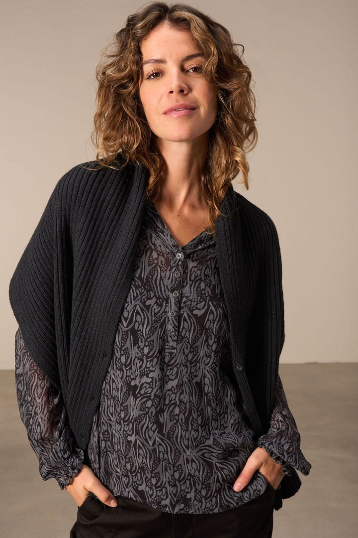 Woman modeling a versatile Foulard cape in black, layered over a patterned top for a stylish look.
