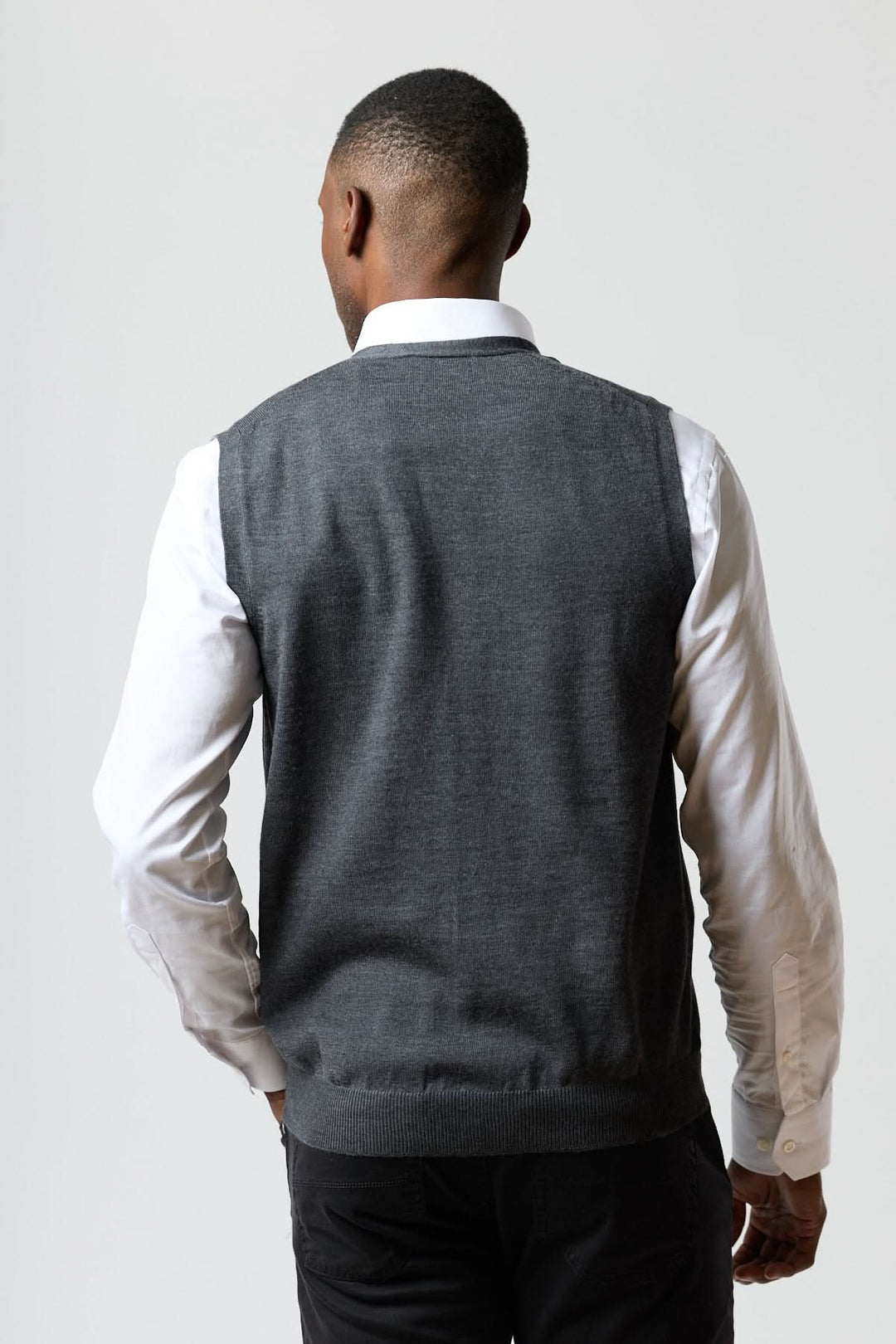 Homme portant un gilet en laine mérinos à col en V de couleur grise, vu de dos, confort et élégance italienne décrits en français.