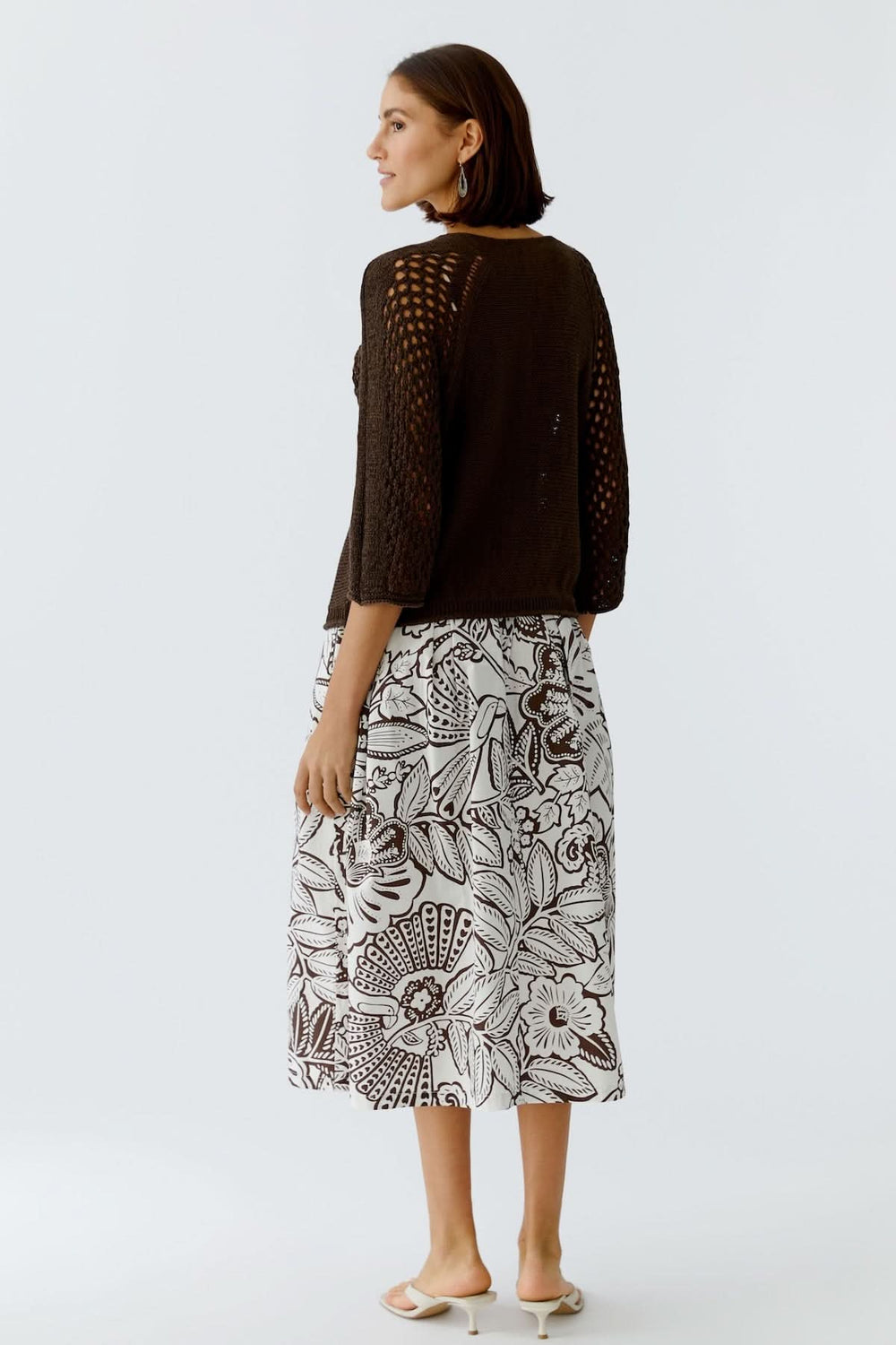 Femme portant un haut coupe moderne épurée avec une jupe à motifs floraux, vue de dos, style minimaliste.