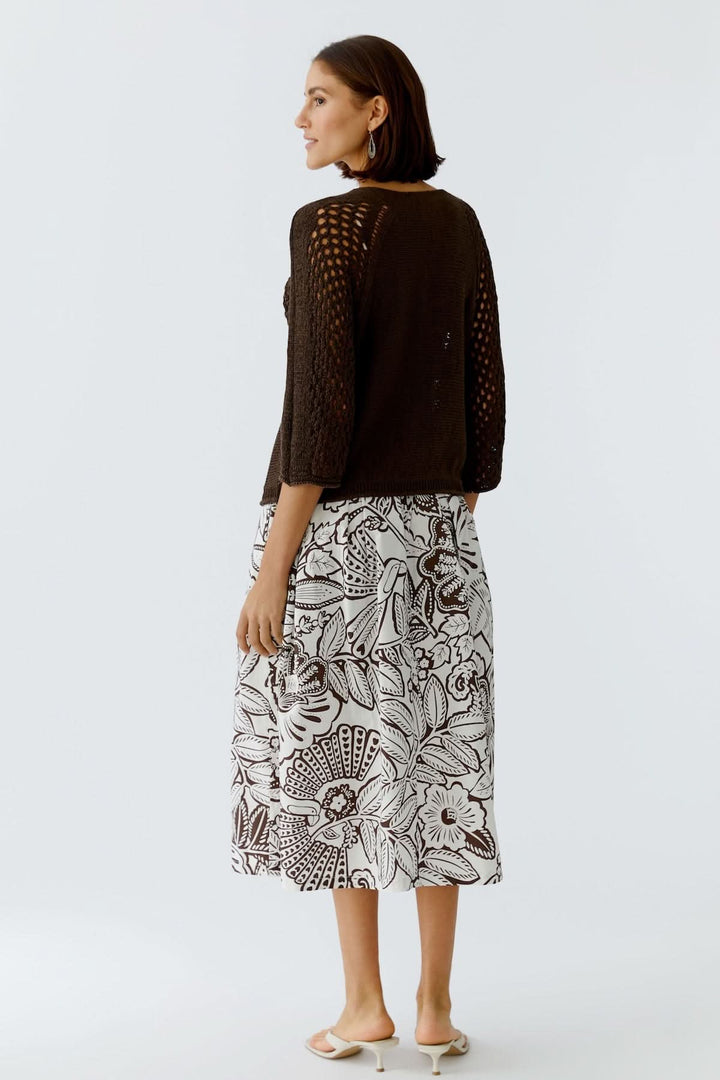 Femme portant un haut coupe moderne épurée avec une jupe à motifs floraux, vue de dos, style minimaliste.