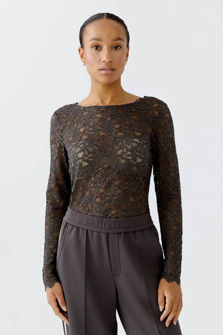 Femme portant un haut en dentelle florale, coupe ajustée avec manches longues et encolure bateau, style élégant et féminin.
