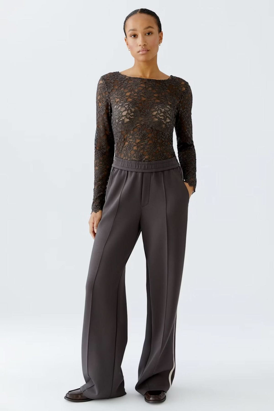 Femme portant un haut en dentelle florale avec encolure bateau et manches longues, combiné avec un pantalon habillé gris.