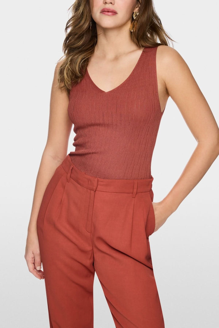 Femme portant un haut en maille côtelée sans manches à col v, élégant et moderne, en tissu extensible, avec un pantalon assorti.