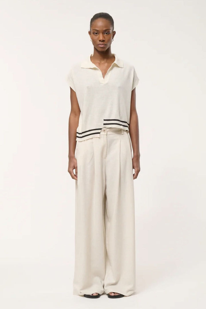 Haut en tricot à rayures contrastantes avec col polo ouvert, ourlet graphique, porté avec pantalon ample, silhouette décontractée moderne.