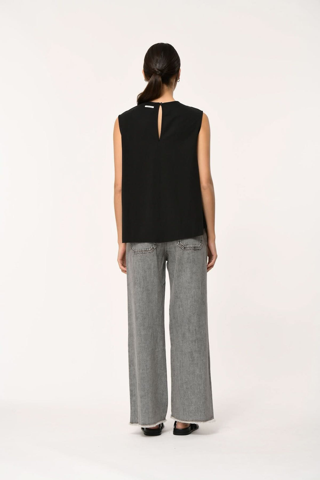 Vue arrière du Haut fluide LORO asymétrique sans manches, tombé léger et coupe contemporaine, porté avec un pantalon gris ample.