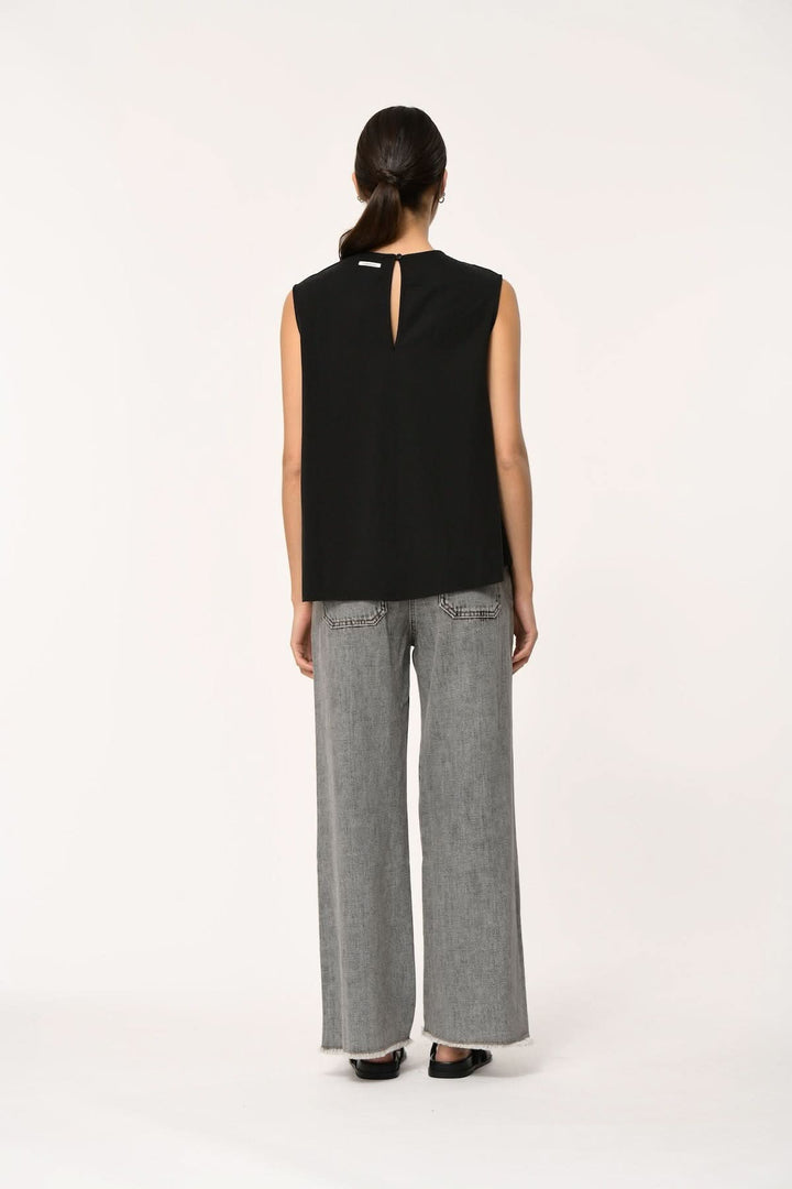 Vue arrière du Haut fluide LORO asymétrique sans manches, tombé léger et coupe contemporaine, porté avec un pantalon gris ample.