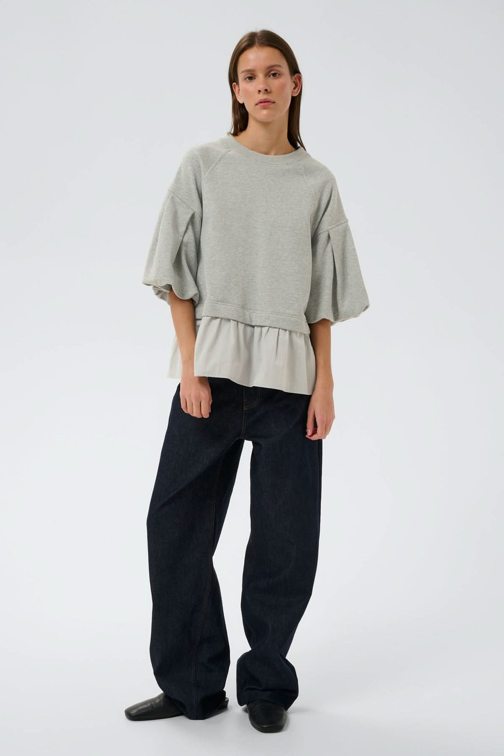 Femme portant un haut ouaté avec ourlet Dessy, coupe ample, manches volumineuses et ourlet plissé, silhouette moderne et confortable.