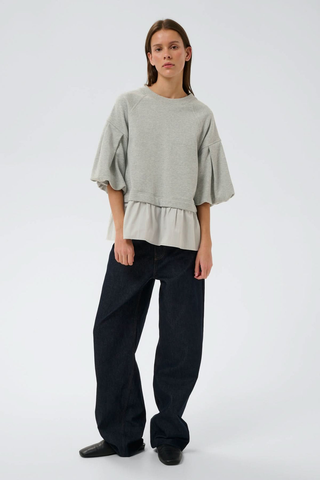 Femme portant un haut ouaté avec ourlet Dessy, coupe ample, manches volumineuses et ourlet plissé, silhouette moderne et confortable.