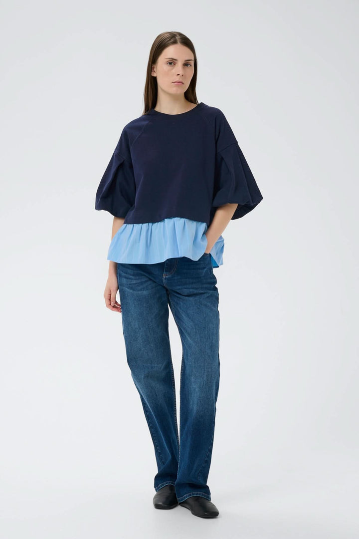 Femme portant un Haut ouaté avec ourlet Dessy, manches volumineuses et ourlet plissé pour une silhouette contemporaine et féminine.
