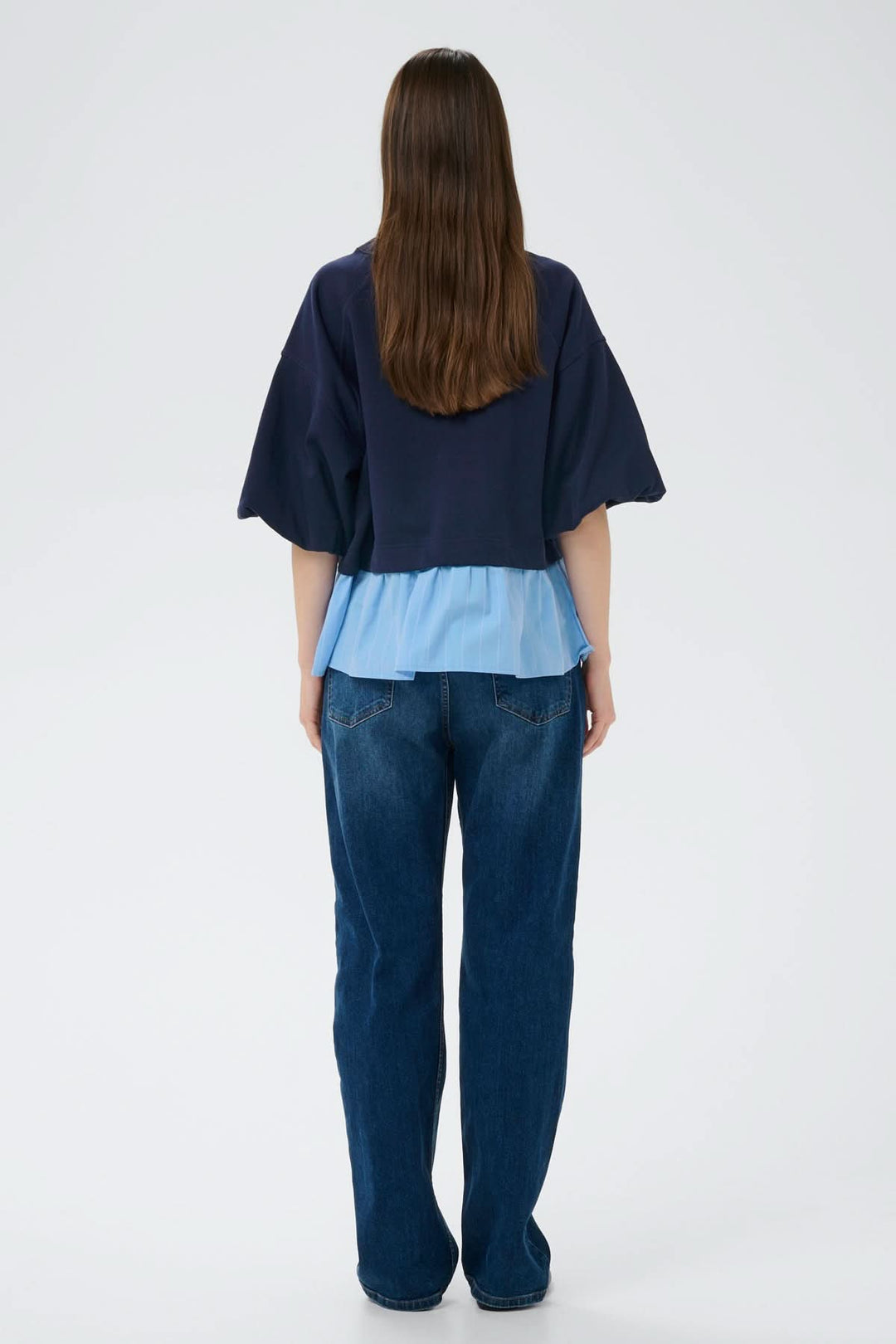 Femme portant un haut ouaté avec ourlet Dessy, silhouette contemporaine avec manches volumineuses et effet superposé, vue arrière.