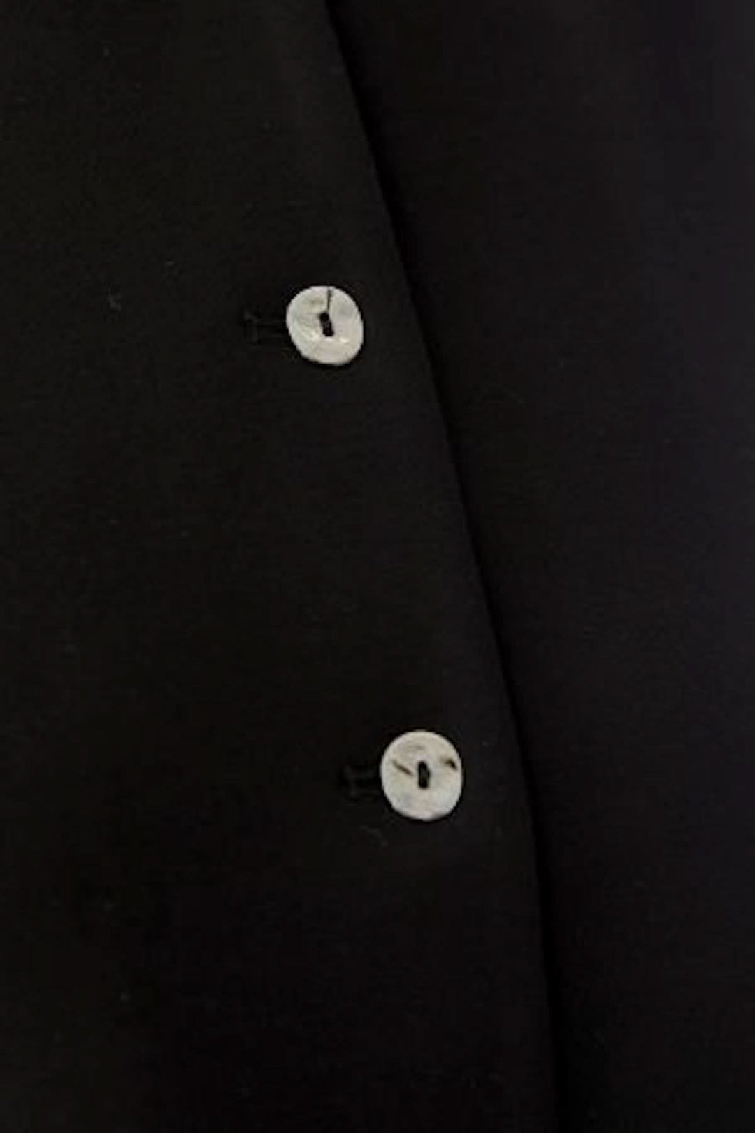 Détail bouton du haut sans manches boutonné, design sobre et élégant en noir, parfait pour une tenue moderne et minimaliste.