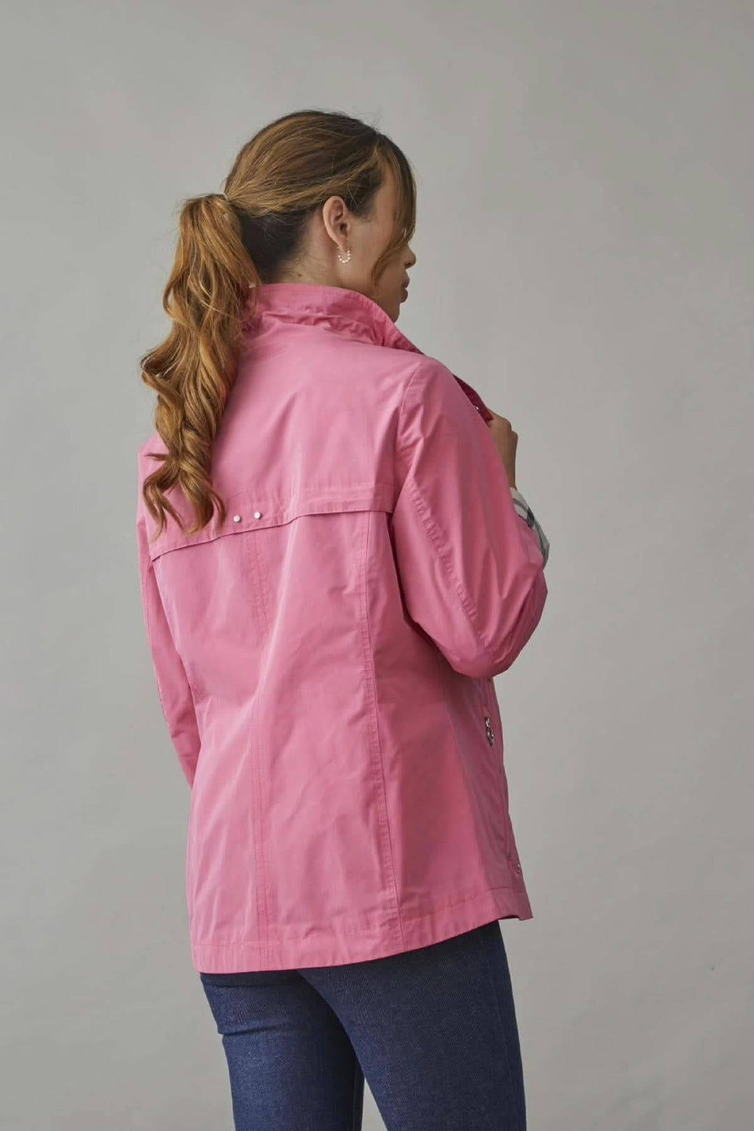 Femme portant un imperméable sans capuchon rose, vue arrière, avec col montant ajustable et coupe décontractée.