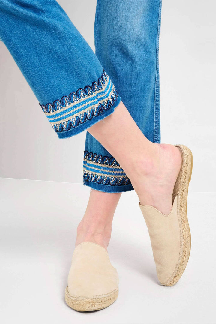 Femme portant des mules beiges avec un jean brodé à la cheville, style décontracté et élégant.