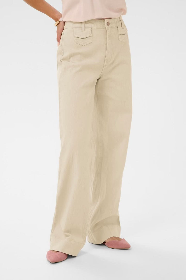 Jean Tilde coupe large taille haute, beige, jambes longues et droites, poches avant, porté avec chaussures roses, style moderne fluide.