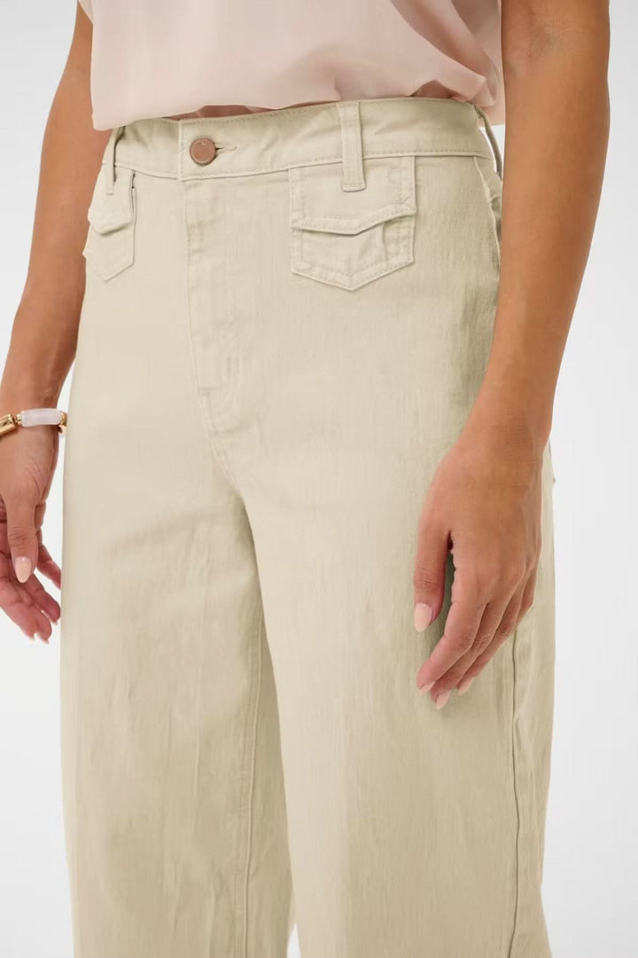 Jean Tilde coupe large taille haute en beige avec poches avant et fermeture à bouton, offrant une allure moderne et confortable.