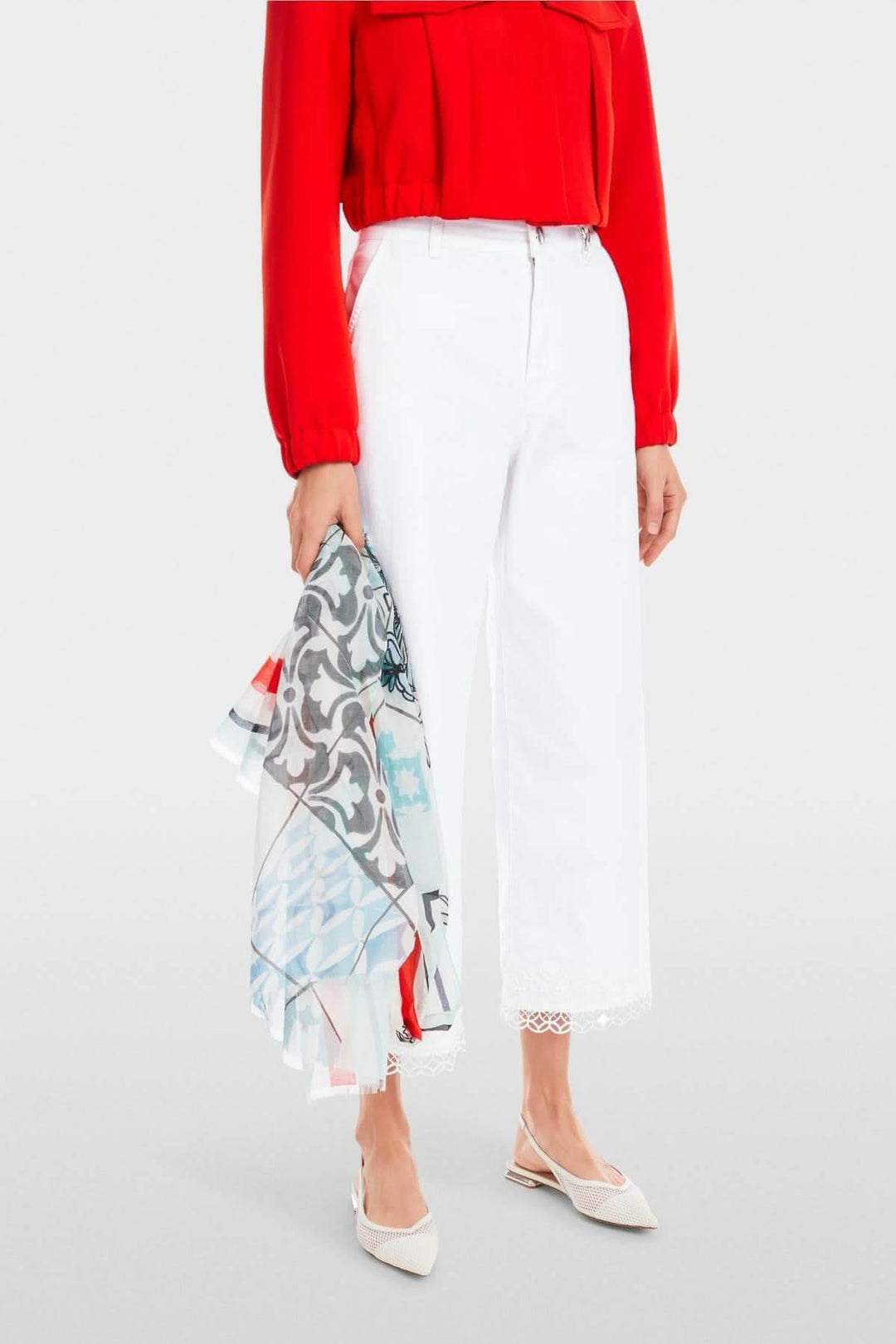 Femme portant un haut rouge et un jean blanc à taille haute avec dentelle, tenant un foulard coloré.