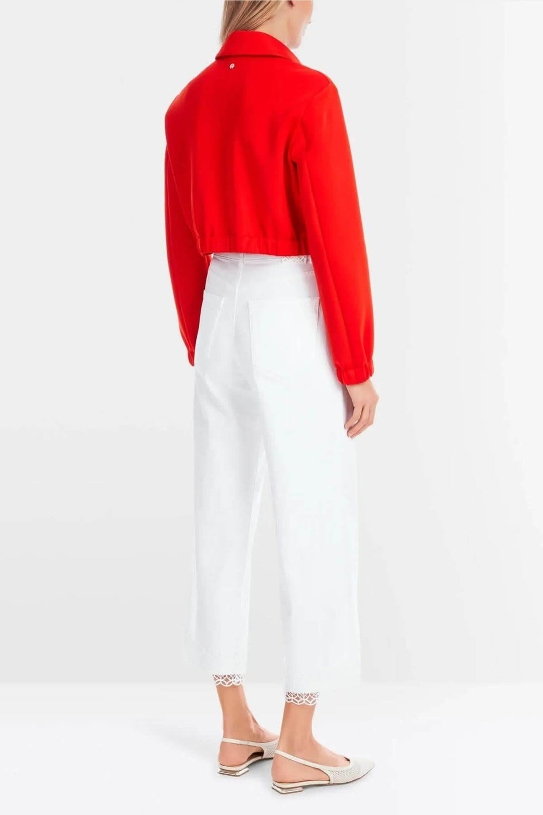 Femme portant une veste rouge et un pantalon blanc avec bordure en dentelle, vue de dos.