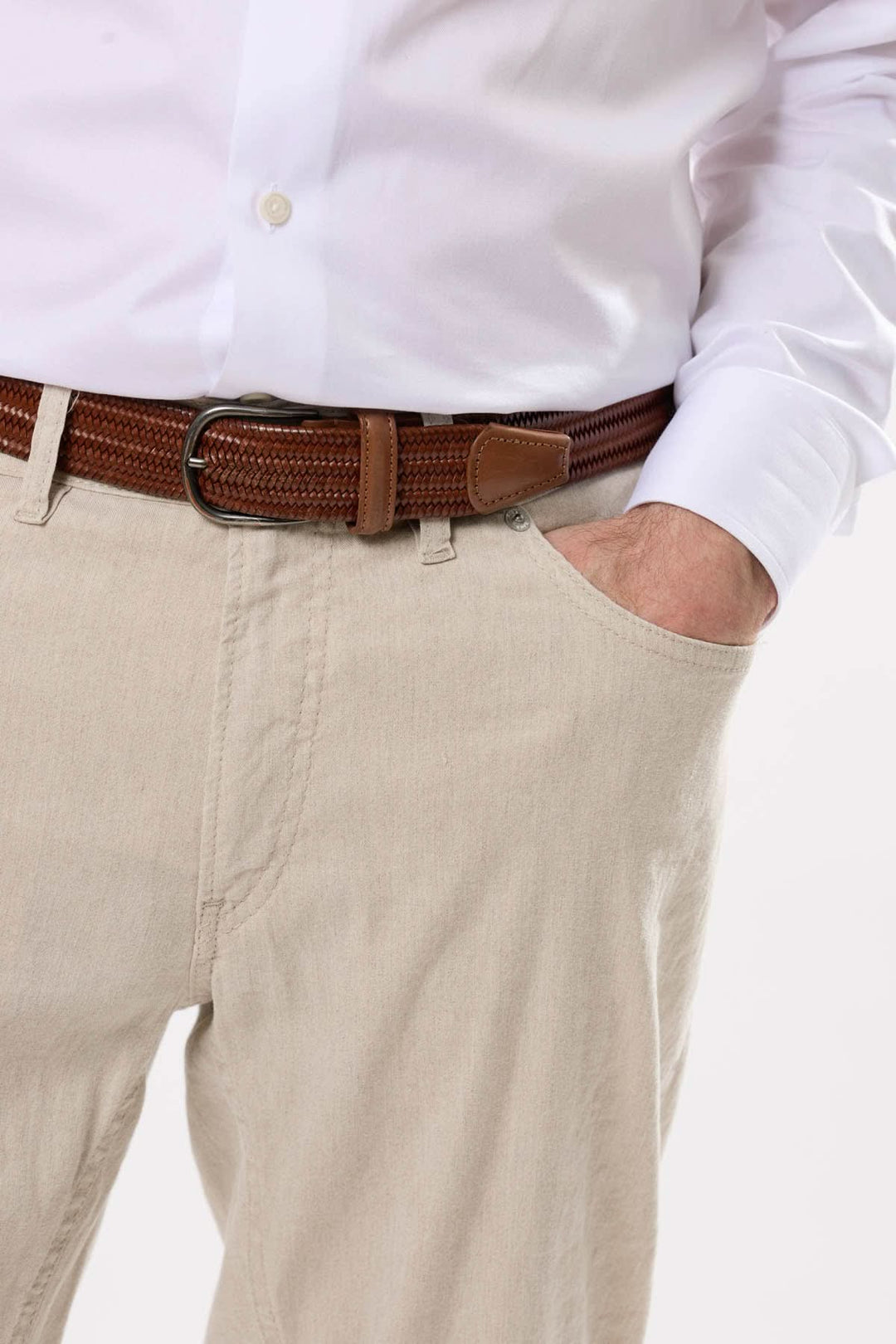 Homme en chemise blanche portant un pantalon beige et une ceinture marron, main dans la poche.