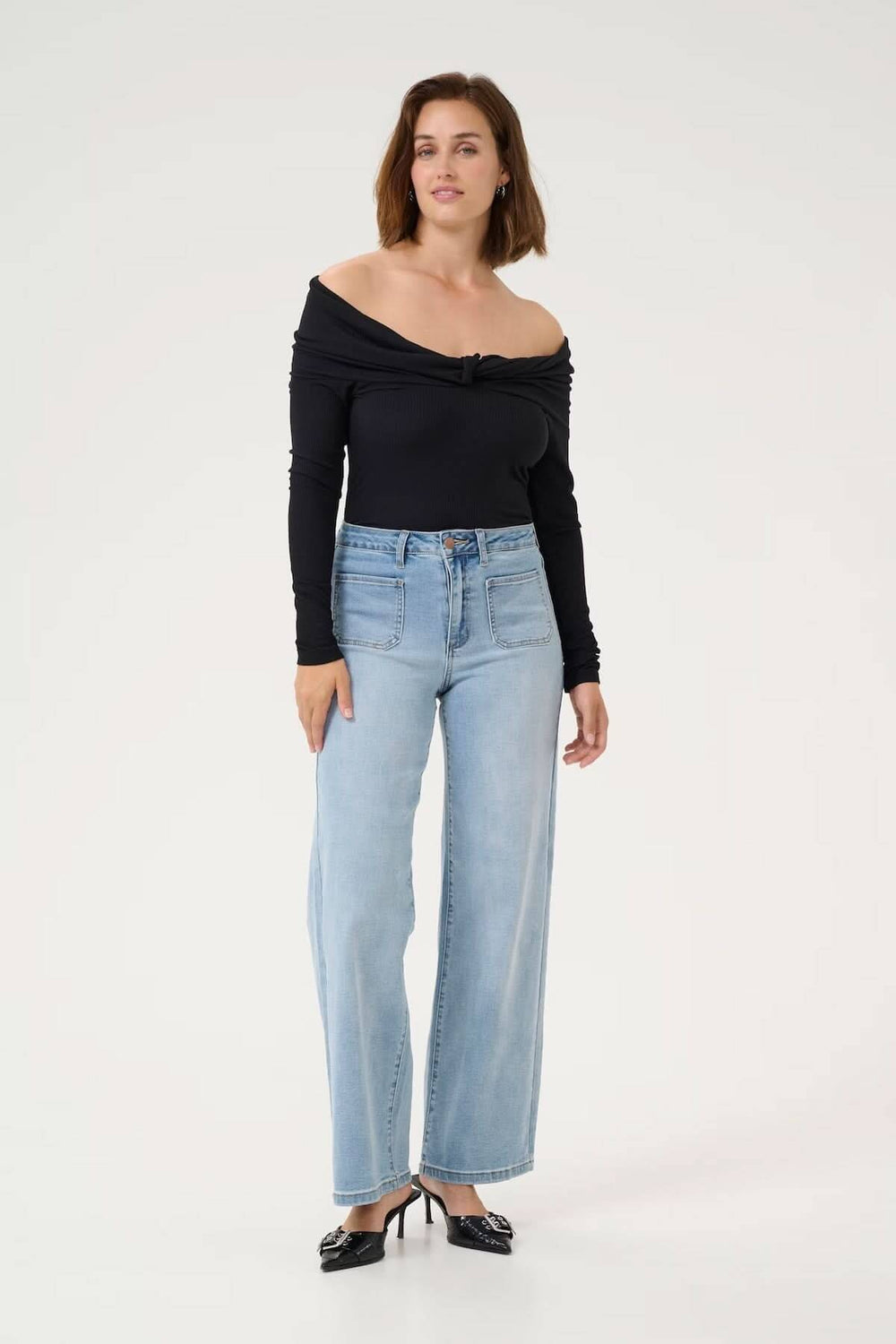 Femme portant un jean à coupe large, taille haute, avec un top noir en décolleté, style moderne et décontracté.