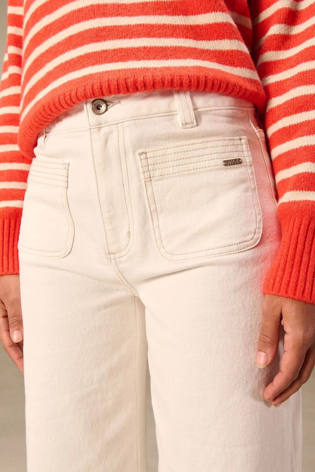 Jean jambe large blanc avec poches appliquées, taille haute et pull rayé rouge, parfait pour un look décontracté et moderne.