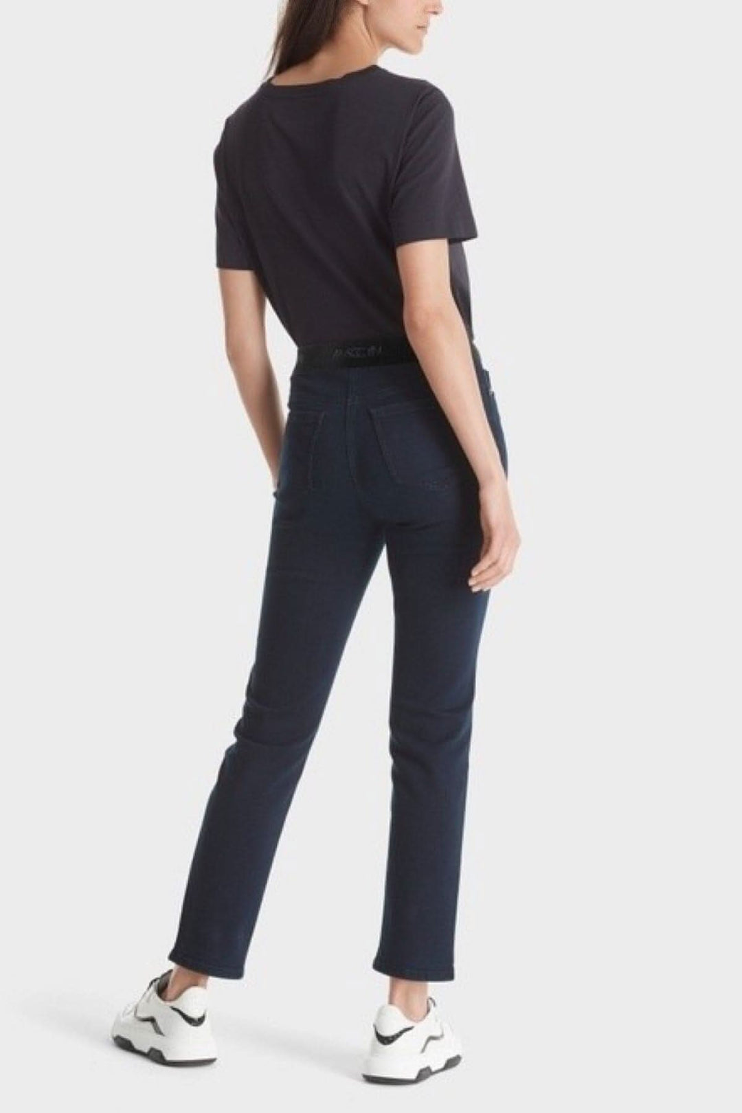 Femme portant des jeans SIENA en coton biologique, vue arrière, avec un t-shirt noir et des baskets blanches.