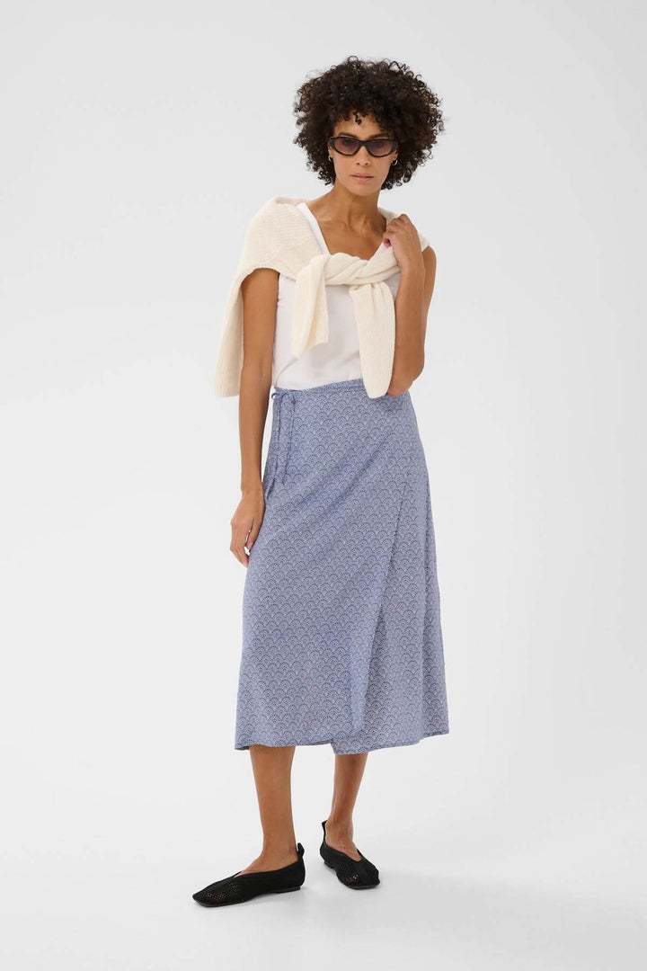 Femme portant la Jupe Arielle bleue, coupe évasée, taille ajustable, avec imprimé délicat, parfaite pour tenues estivales.