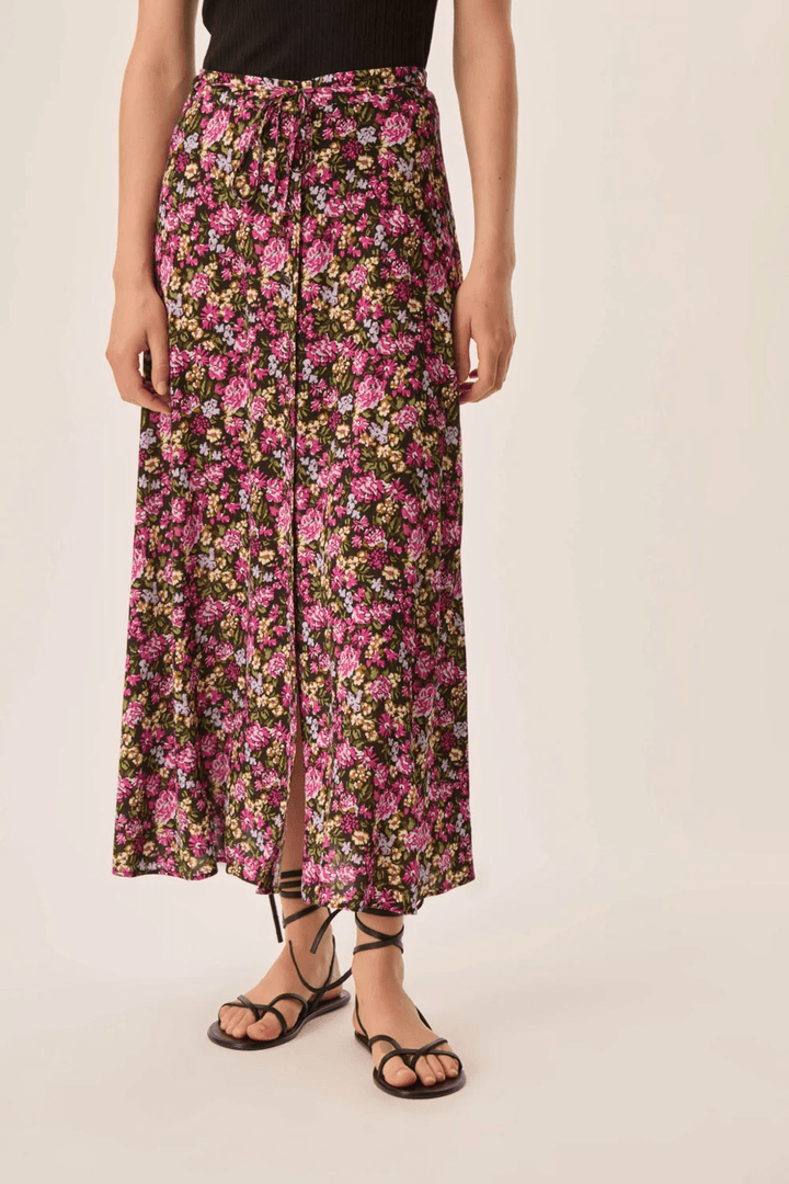 Jupe Elizette longue fluide à taille nouée rose avec imprimé floral, fente avant, portée avec des sandales.