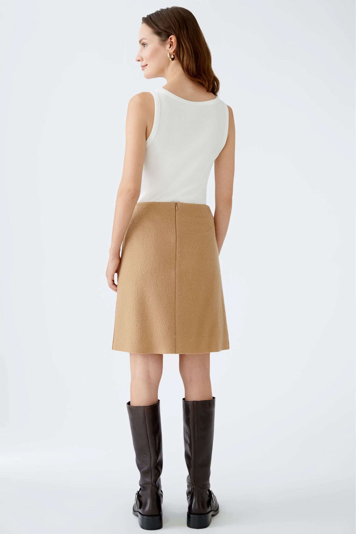 Femme portant une jupe courte en lainage, taille haute, coupe droite évasée, associée à des bottes hautes, style élégant.