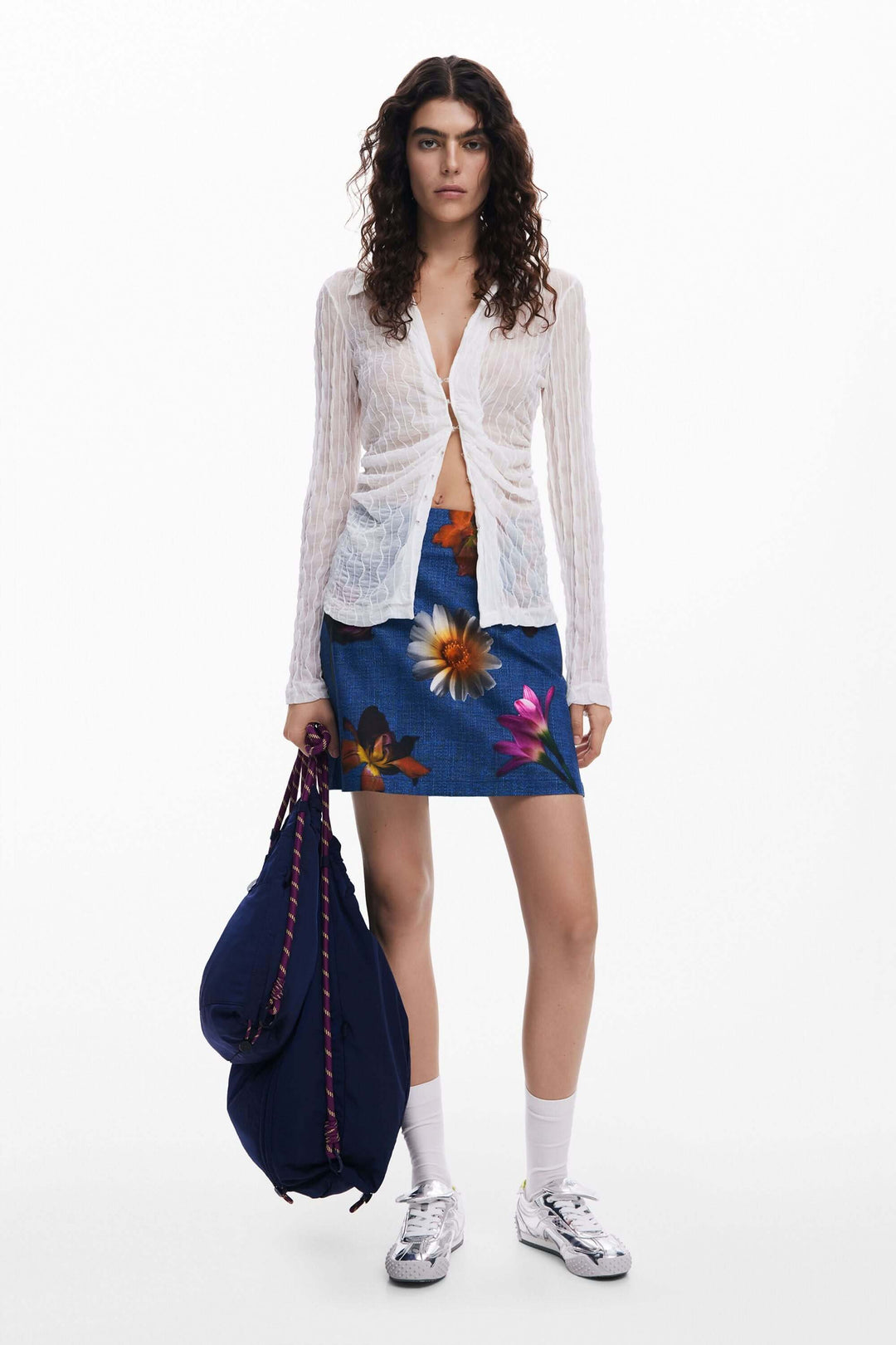 Femme portant une jupe courte à fleurs et un cardigan, avec un sac à dos, idéale pour un look estival.