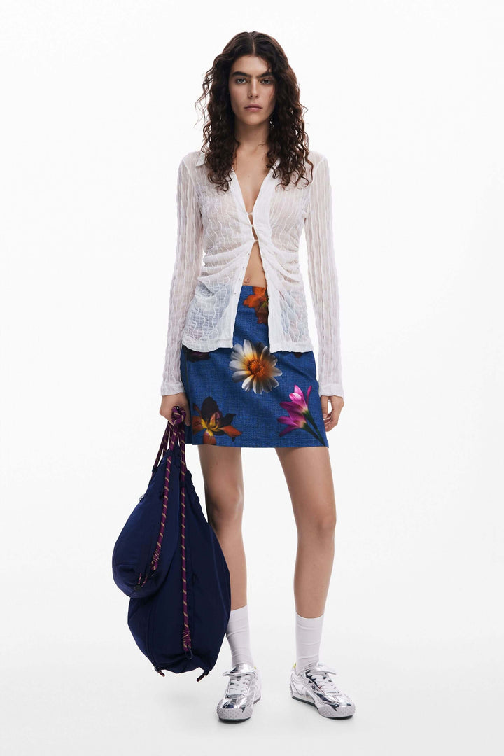 Femme portant une jupe courte à fleurs et un cardigan, avec un sac à dos, idéale pour un look estival.