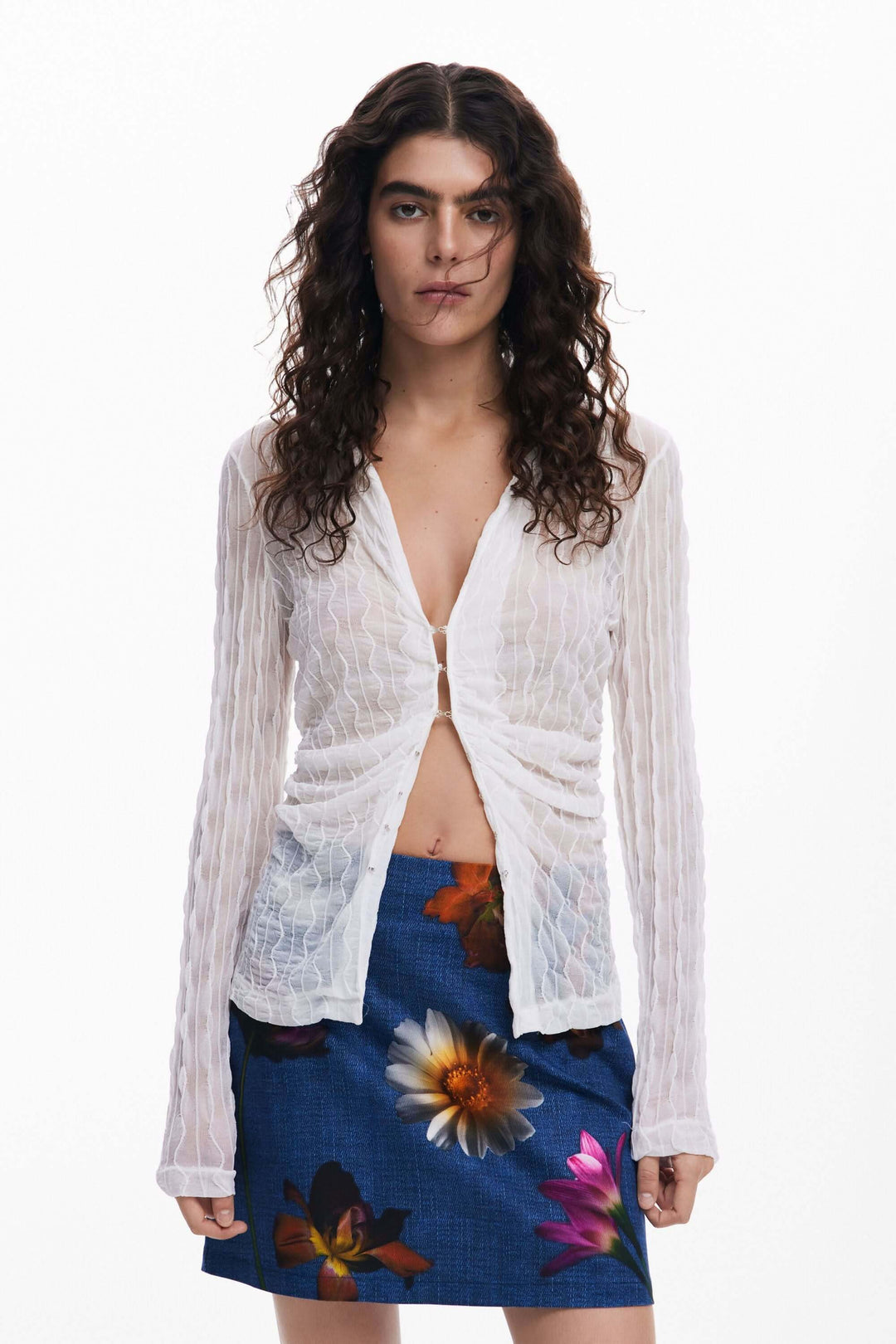 Femme portant un haut blanc et une jupe courte à fleurs colorées, style décontracté et estival.