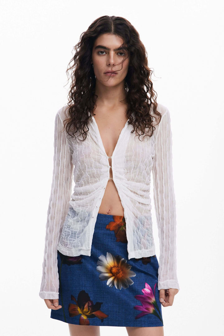 Femme portant un haut blanc et une jupe courte à fleurs colorées, style décontracté et estival.