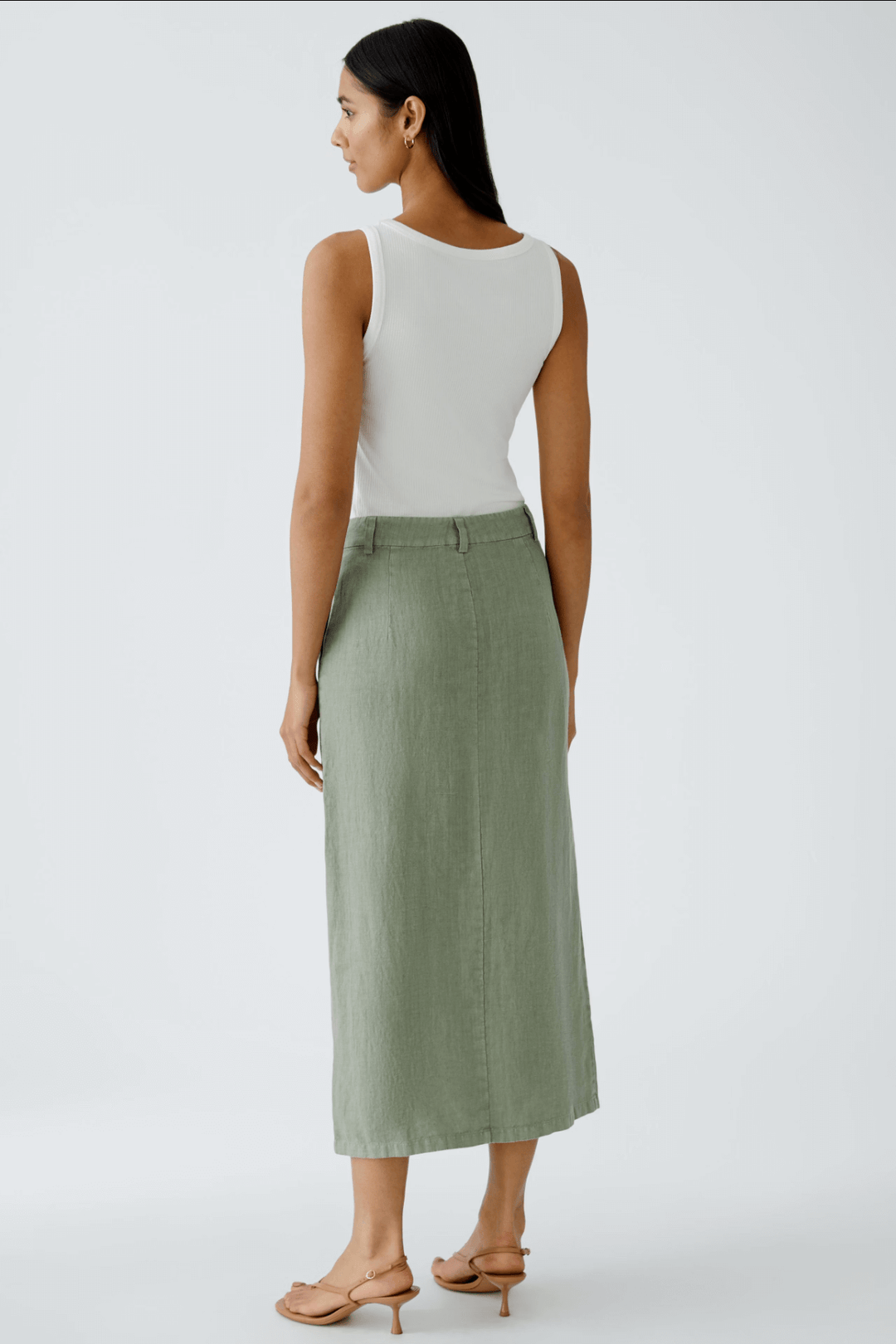 Femme portant une jupe longue en lin olive, vue de dos, avec débardeur blanc et sandals, élégance décontractée.