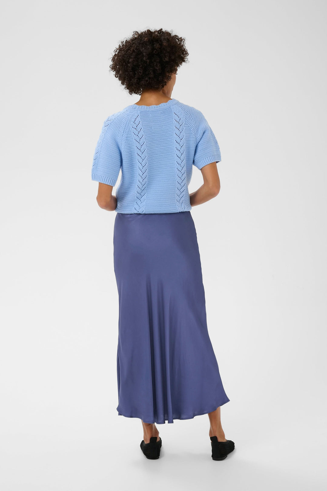 Vue arrière de la Jupe midi Laurina en satin fluide, bleu, portée avec un pull tricot bleu, créant une allure élégante et naturelle.